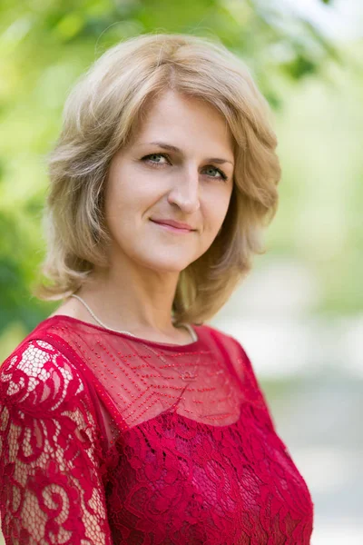 European woman 40 years old in a red dress on the nature. Portrait of a middle aged woman.