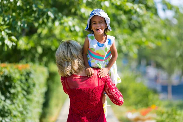 Beyaz bir kadının zenci bir kız omuzunda taşır. Avrupa anne ve üvey kızı esmer yürüyüşe eğlenin.