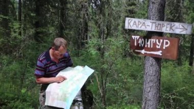 Turist işaretleri yakınındaki bir harita. Yazıtlar tüngür Köyü, Kara Turek dağ. Bir adam gezgin bir zam kayboldum ve harita üzerinde bir yol arıyor.