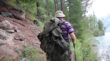 Bir adam bir sırt çantası ile bir dağ nehir boyunca girer. Bir turist sırtında büyük bir çanta ile gürültülü bir hızlı Nehri yakınında kayalar boyunca yürür.