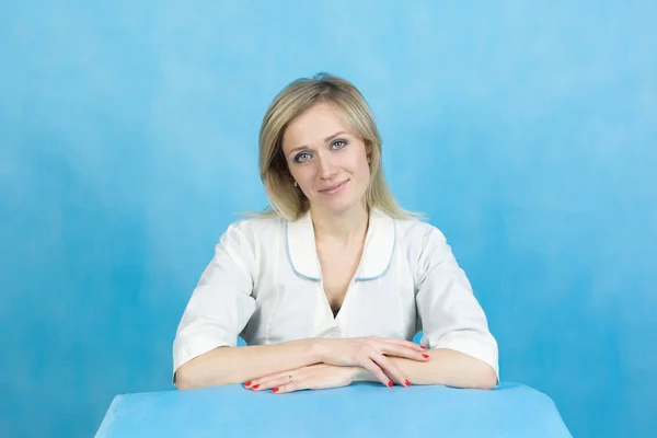Girl lab technician on a blue background. Woman in a white lab technician doctor sits at the table on a blue background.