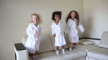 Üç küçük kız kanepede atlama vardır. Beyaz kat olarak farklı milletlerden kızlar dans ve bir banyodan sonra gülmek.