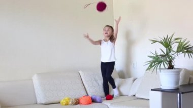 Çocuk iş parçacığının biriktiricileri toplarla oynuyor. Bir kız kanepede standları ve yün iplik topları atar.