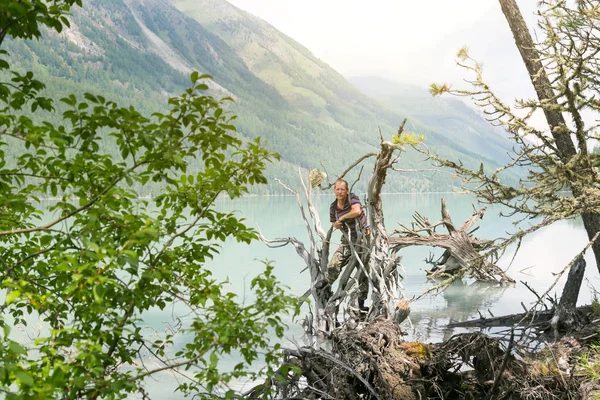 A man stands on a fallen tree in the water. A tourist stood on the trunk of a tree fallen from the wind in a mountain lake.