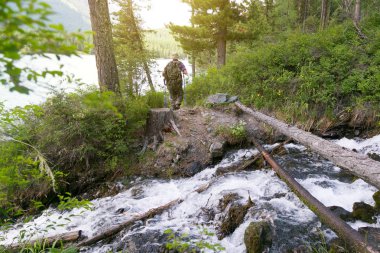 Turistik günlük nehrin karşısına geçti. Bir ağaç ve bir hızlı dağ dere bir adam gezgin duruyor.