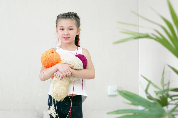 A girl with balls of thread for knitting. The little girl holds knitting yarns in her hands, and the yarn hangs on her head.