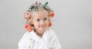 Saçında curlers saç tokaları ile kız. Beyaz önlük, küçük bir kız pembe curlers saçları bükülmüş..