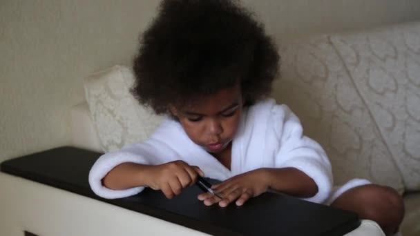 小非洲裔美国女孩在手上画钉子 一个穿白色晨衣的3 4岁女孩坐在沙发上 用清漆画指甲 — 图库视频影像