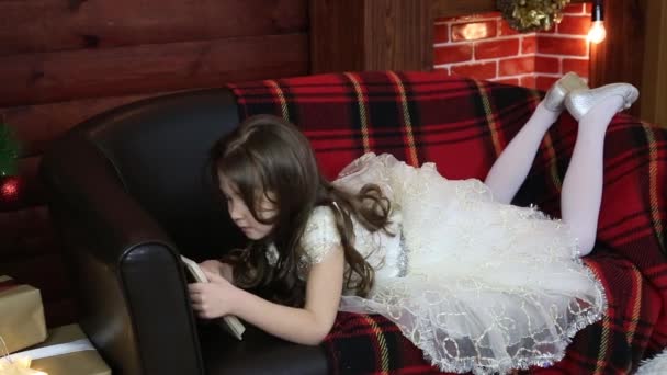 Uma Rapariga Ler Livro Deitada Sofá Uma Menina Vestido Festivo — Vídeo de Stock