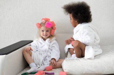 Siyah kız arkadaşıyla saç curlers kilitleniyor. Afro-Amerikan kadın beyaz arkadaşı kafasında saç pins takılır.