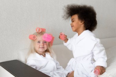 Siyah kız arkadaşıyla saç curlers kilitleniyor. Afro-Amerikan kadın beyaz arkadaşı kafasında saç pins takılır.