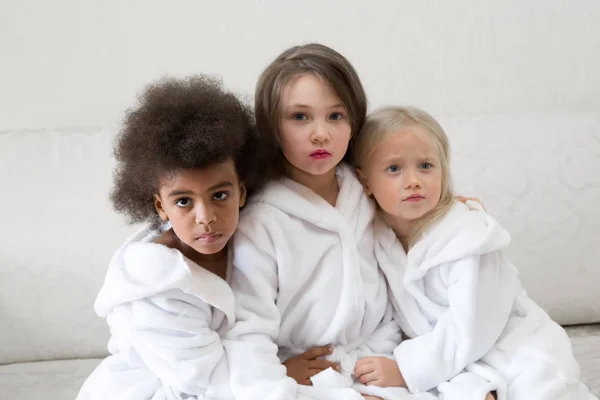 Children girls with painted lips. Little girls in white coats play makeup with thick lipstick on their lips.