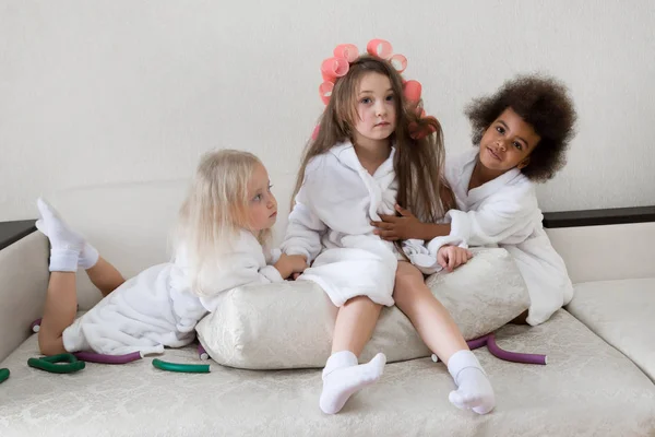 Girls girlfriend 5 years of age in white coats. Three sisters hug sitting on the couch.