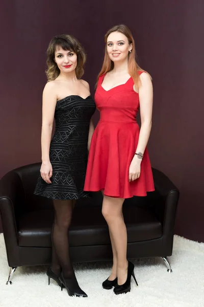 两个穿红色和黑色衣服的女孩在黑暗的背景下在公寓里 最好的朋友背对着对方站着 — 图库照片