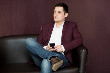 20-25 yaşında bir adam siyah saçlı bir takım elbiseli bir telefon tutuyor.