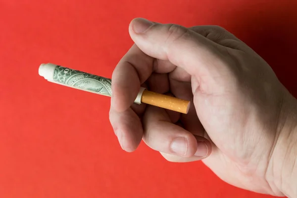 A hand is holding a cigarette rolled into a dollar bill.