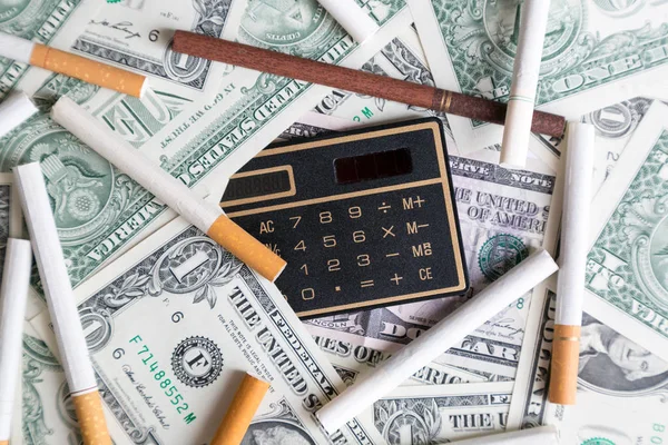 Hesap makinesi ve sigara bir tomar para üzerinde yalan.