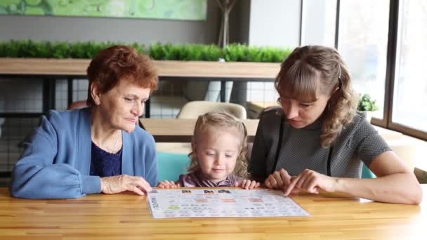 祖母の娘と孫娘のカフェでメニューを見ています 女性の孫娘の母と祖母がレストランでメニューを見ての つの世代の女性の家族 — ストック動画