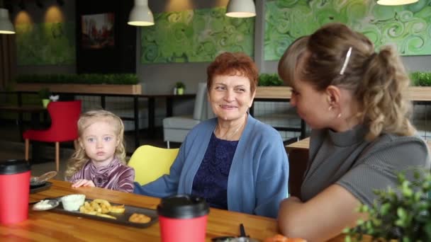 祖母は孫娘に物語を伝える 年配の引退した女性がカフェで彼女の小さな女の子の孫娘に物語を伝えます — ストック動画