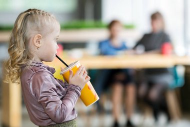 Küçük bir çocuk tek başına küvetten bir kokteyl içiyor ve anne ve büyükanne arkadan konuşuyor. Gözetimi olmayan bir çocuk, ebeveynlerin kayıtsızlığı.