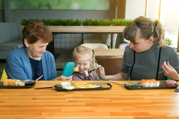 Mom and grandmother feed the little girl together. The child does not want to eat there, but his parents force him to eat.