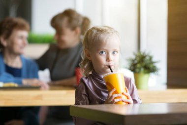 Kız annesinin ve büyükannesinin arka planında meyve suyu içiyor..