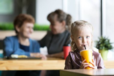 Kız annesinin ve büyükannesinin arka planında meyve suyu içiyor..