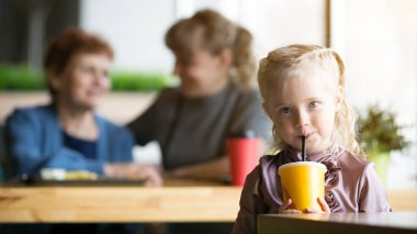 Kız annesinin ve büyükannesinin arka planında meyve suyu içiyor..