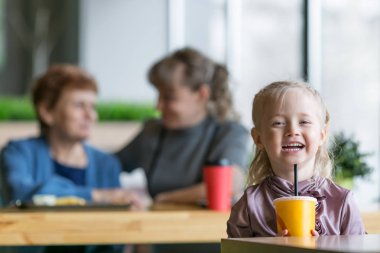 Kız annesinin ve büyükannesinin arka planında meyve suyu içiyor..