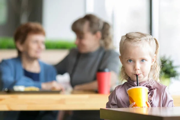 Het meisje drinkt SAP op de achtergrond van zijn moeder en grootmoeder. — Stockfoto