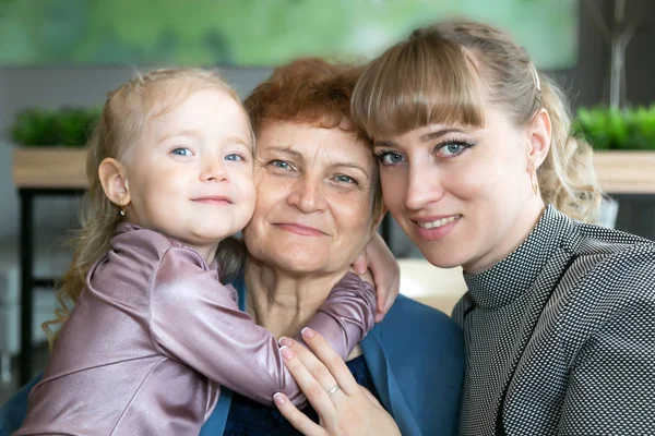 Daughter and granddaughter hug and kiss grandmother. A little girl and a young woman hug their elderly mom and grandmother tightly.