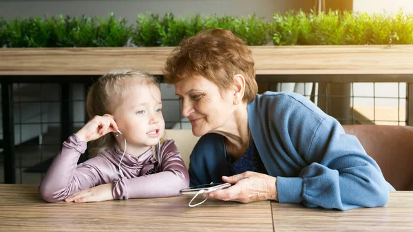 Abuela llevaba auriculares a su nieta para escuchar el cuento de audio . — Foto de Stock