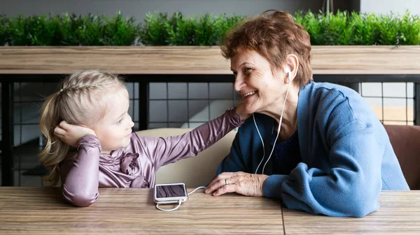 Abuela llevaba auriculares a su nieta para escuchar el cuento de audio . — Foto de Stock