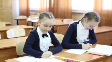 Kız kız öğrenci bir not defterinde birbirlerini gözetlerler. Kız öğrenciler derste sınıfta kontrol çalışmaları sırasında bir not defteri birbirlerine bakmak