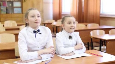 Liseli kız öğretmenin sorusuna cevap vermek için elini kaldırır. Bir genç kız iki kız masada oturuyor, bir öğrenci öğretmenin sorusuna cevap vermek için elini kaldırır, ikinci kız ders dersinin konusunu bilir.