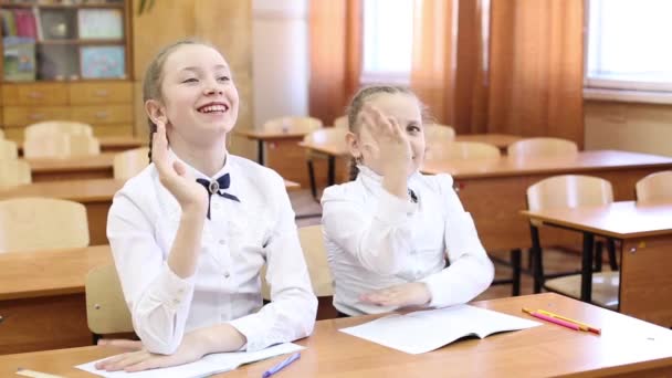 女子高生は先生の質問に答えるために手を上げる ティーンエイジャーの女子高生の2人の女の子がテーブルに座って 一人の生徒が先生の質問に答えるために手を上げ 2番目の女の子はレッスンの主題を知っています — ストック動画