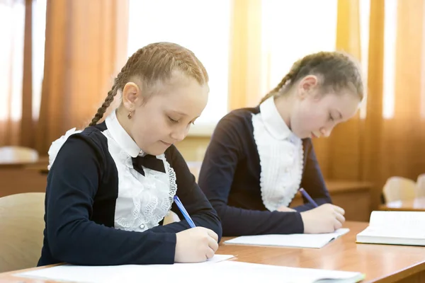 Дети пишут, сидя за школьным столом . — стоковое фото