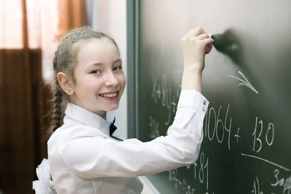 Dziewczyna kobieta uczeń szkoły podstawowej pisze na tablicy. — Zdjęcie stockowe