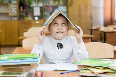 Bir kız öğrenci bir ders kitabı koydu, kafasına bir defter bir defter çalışmaları ile ilgili sorunlara karşı koruma olarak çatılı bir ev yaptı Kız bir kitaptan başını bir çatı ile bir ev yaptı.