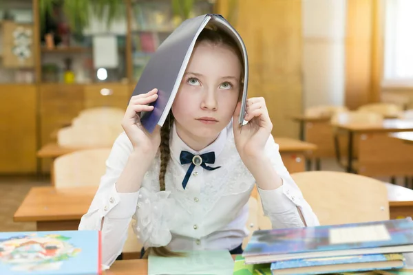 The girl made a house with a roof on her head from a book, with a roof as protection against problems with studies. A schoolgirl put a textbook, a book a notebook on her head made a house.