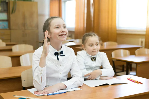 孩子们坐在学校里 一个人举手 女学生举手回答老师的问题 第二个女孩不知道答案 — 图库照片