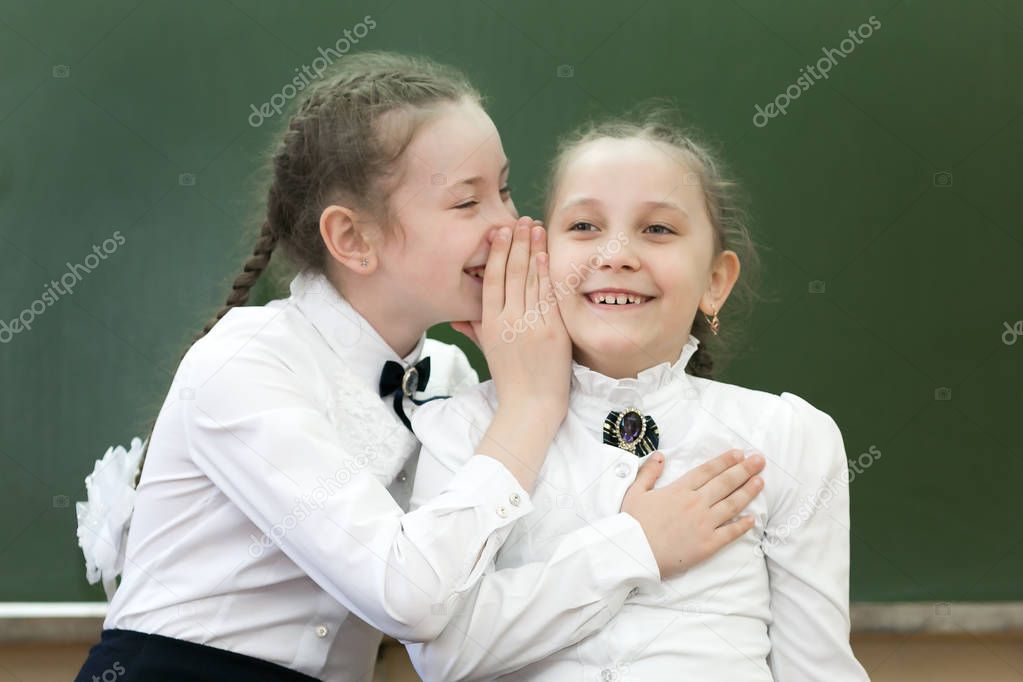 Schoolgirls classmates share their secrets of secrets telling a whisper in his ear near the blackboard in office.