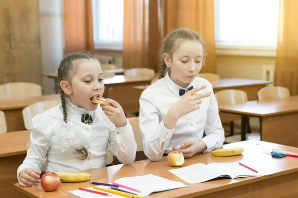 Dwie uczennice jedzą na ławce w klasie. — Zdjęcie stockowe