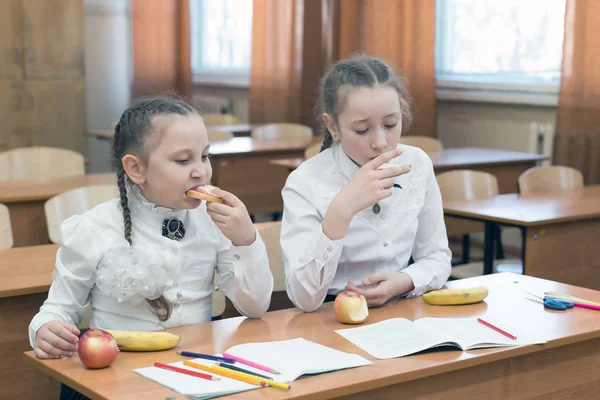 Dwie uczennice jedzą na ławce w klasie. — Zdjęcie stockowe