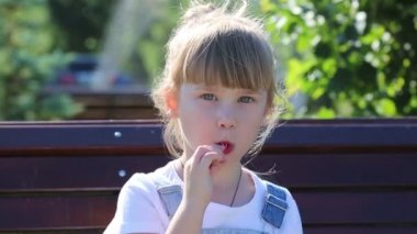 Elinde şeker olan bir çocuk yaz çeşmesinin arka planında. Küçük bir kız bir çeşme arka plan aleyhine bir şehir parkında bir bankta otururken büyük bir tatlı şeker berbat.