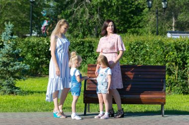 Kadın arkadaşlar 35-40 yaş ve küçük kızları 4-5 yaş parkta konuşuyor.