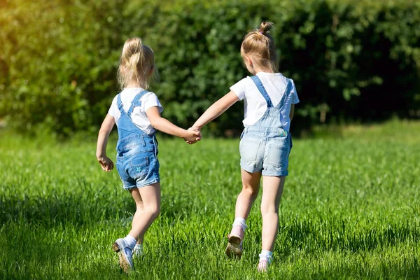 Dzieci biegną na zielonej trawie trzymając ręce. — Zdjęcie stockowe
