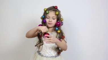 Noel süsleri olan kız kafasını. Küçük bir kız saçlarında ağaç süslemek için Noel topları örgülü, elinde iki güzel topları tutar.