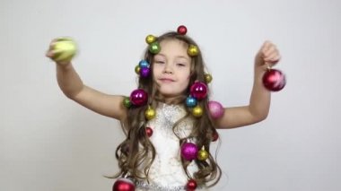Kafasında Noel süsleri olan bir kız. Küçük bir kız saçlarında ağacı süslemek için Noel topları örgülü elinde iki güzel topları tutar.