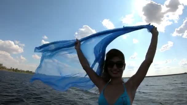 海岸に大きなスカーフを持つ細い女の子 女性は川の近くに現像スカーフパレオを風に抱く — ストック動画